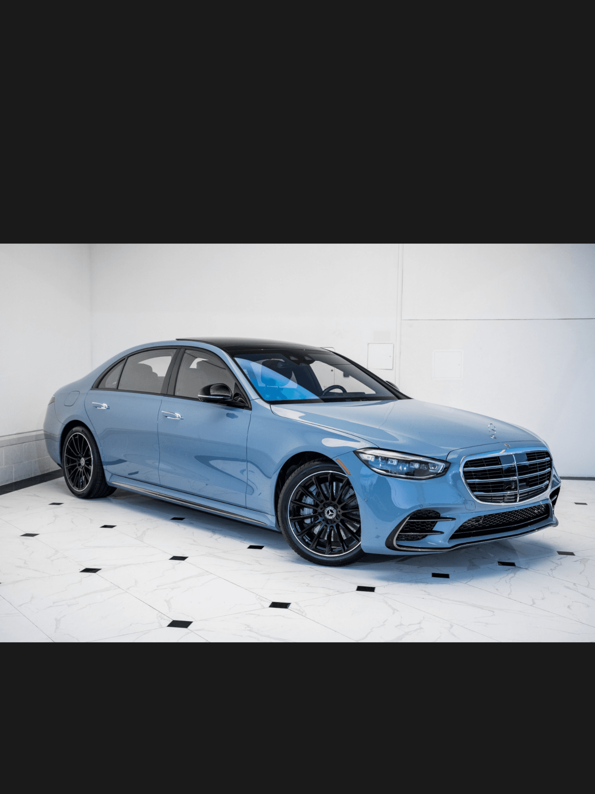 A light blue Mercedes-Benz S-Class sedan with black wheels parked in a bright showroom.