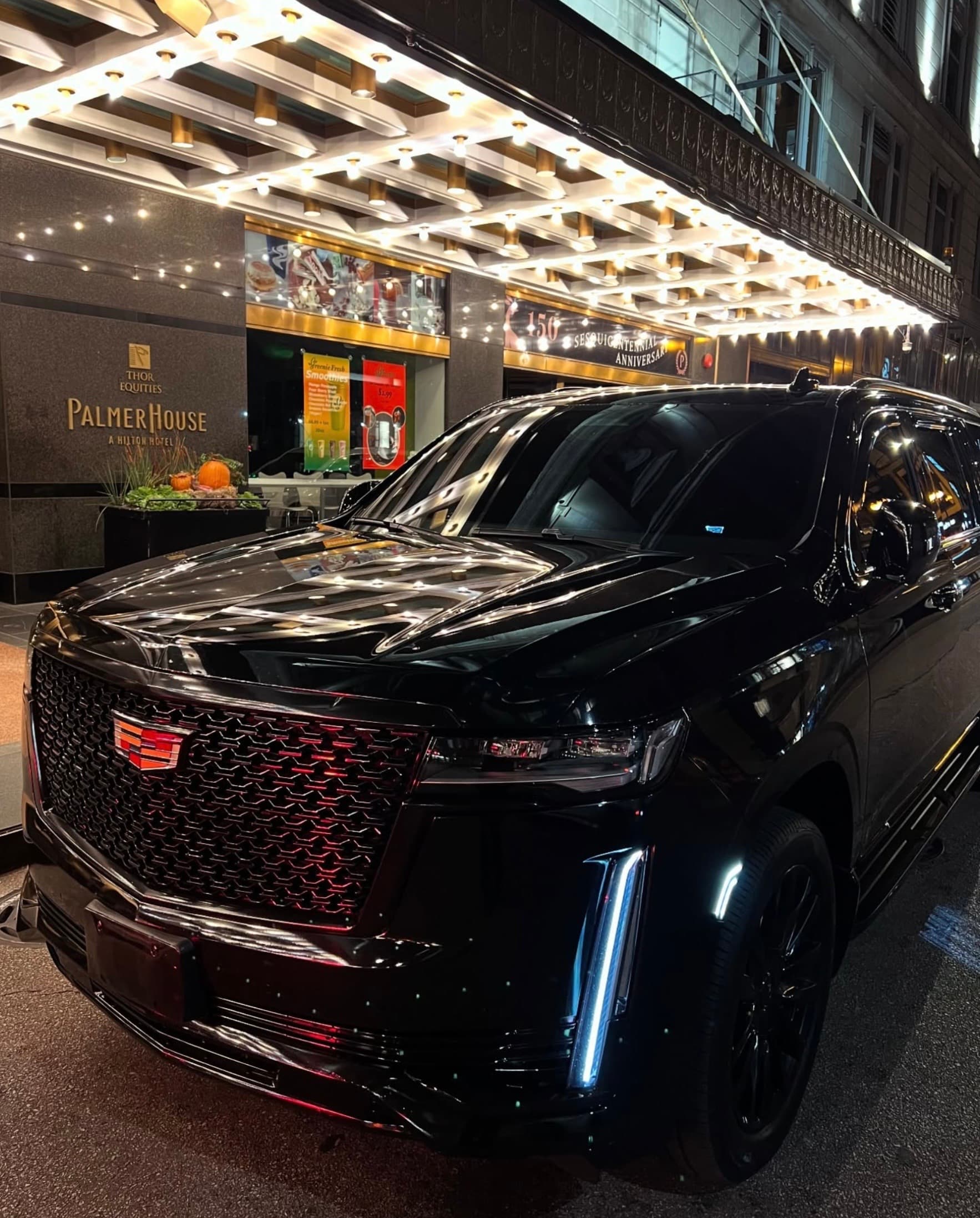 Shiny black Cadillac Escalade parked outside the illuminated Palmer House hotel entrance at night.