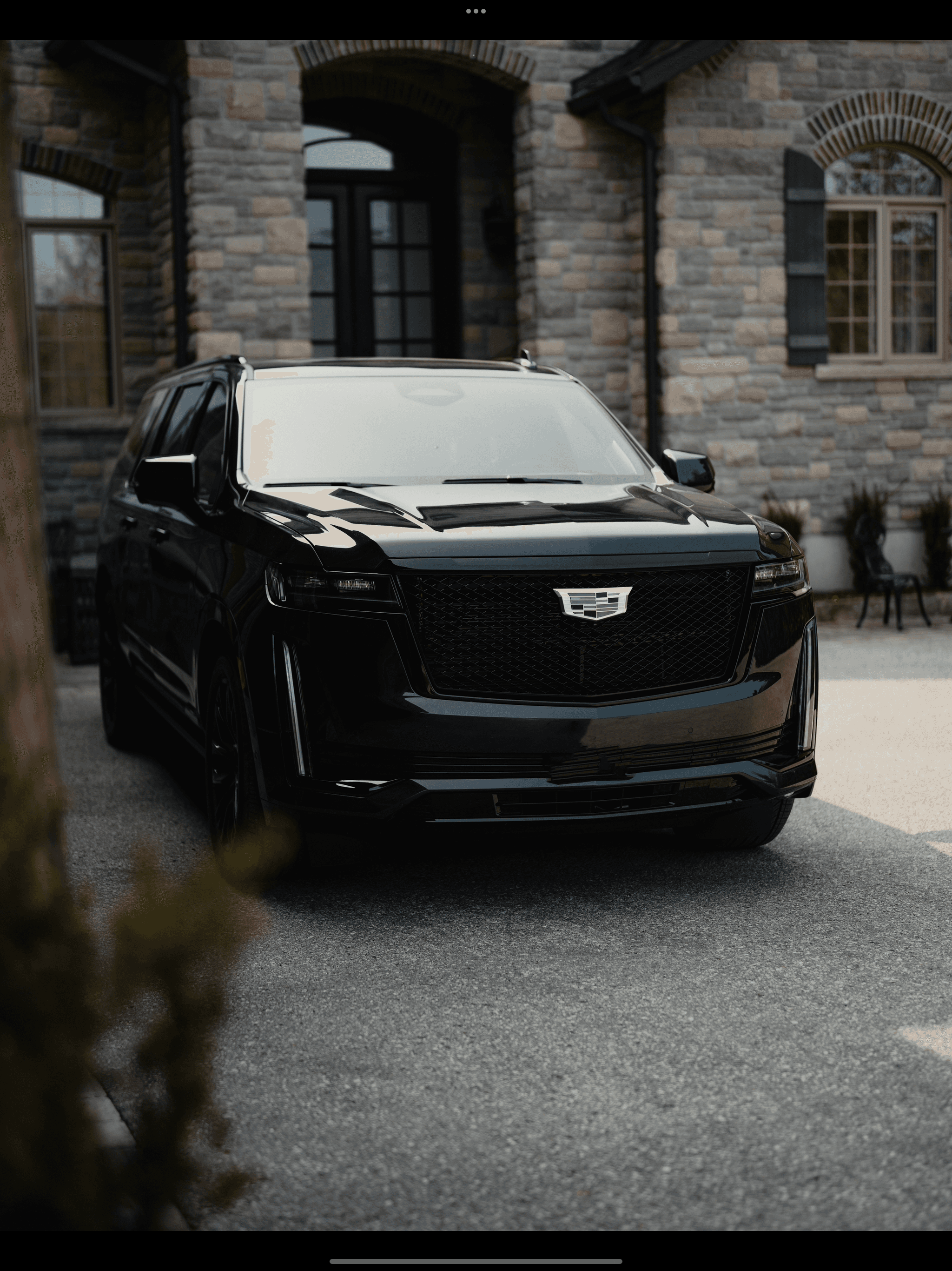 Sleek black Cadillac Escalade parked on a driveway in front of a stone house.
